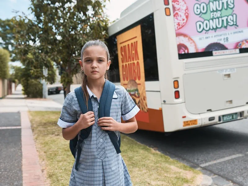 School girl in uniform in front of a bus with unhealthy food advertising on it