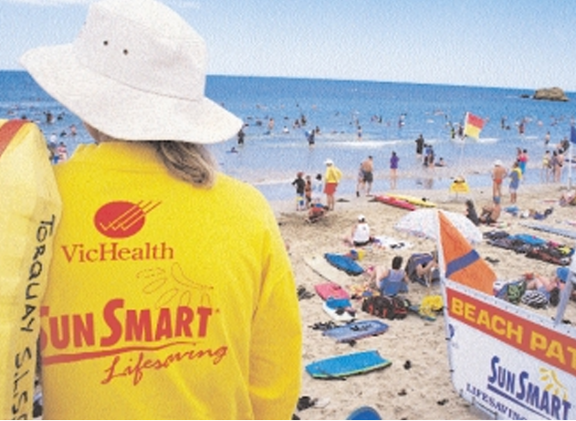 Back of a lifeguard wearing a yellow shirt with the words "VicHealth - Sun Smart - Lifesaving