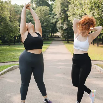 Two women outside in a park stretching and exercising.