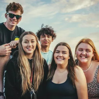Five young adults are at the beach, smiling to the camera. 