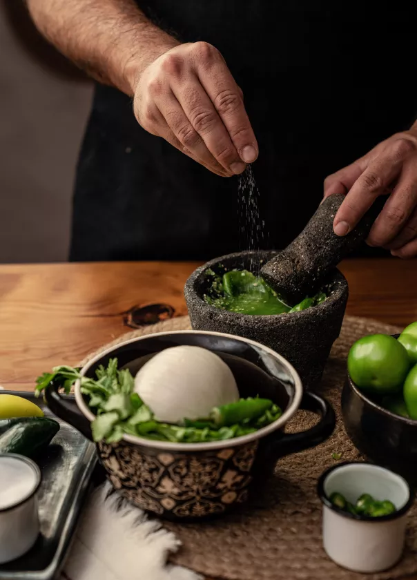 Close up of hands making a green sauce using a mortar and pestle. 