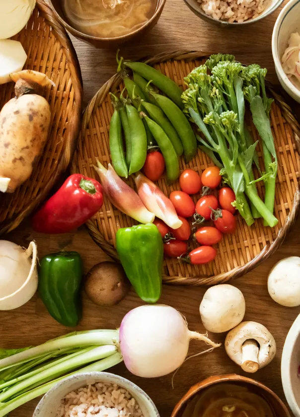 Bird's eye view of vegetables spread out on a table. We see tomatoes, capsicum, onions, mushrooms, carrots, potato, beans and radish. 