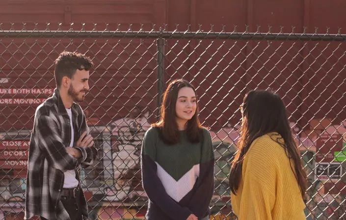 3 young people standing next to a fence and talking to each other