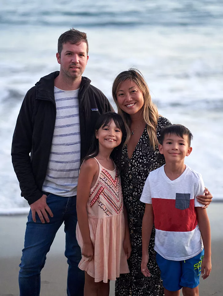 A family with two kids are standing on the beach looking at the camera.