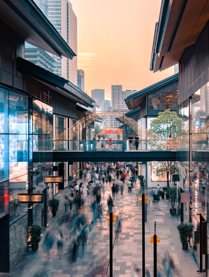 Two buildings are on either side of the image. On the street below we can see blurry figures going about thier shopping. 